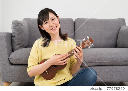 ソファーの前でウクレレを演奏する女性 77978240