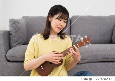 ソファーの前でウクレレを演奏する女性 77978241