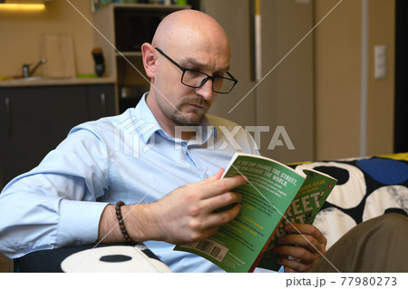 man in casual clothers relaxing and reading book on couch at home. free time activities. Omsk, Russia, 12.10.2020 77980273