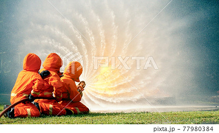 Firefighter fighting with flame using fire hose chemical water foam spray engine. Fireman wear hard hat, body safe suit uniform for protection. Rescue training in fire fighting extinguisher Firefighter fighting with flame using fire hose chemical water foam spray engine. Fireman wear hard hat, body safe suit uniform for protection. Rescue training in fire fighting extinguisher 77980384