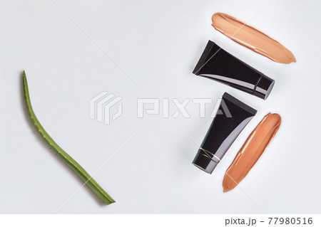Two black tubes of tone cream, foundation smeared by surface, green leaf of aloe isolated on white. Cosmetic packaging. Close up, copy space 77980516