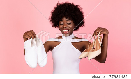 Black Female Choosing Trendy Shoes Holding Sneakers And High-Heels, Studio Black Female Choosing Trendy Shoes Holding Sneakers And High-Heels, Studio 77981485