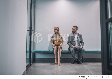 Man and woman with documents sitting in office corridor 77981653