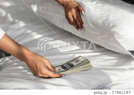Black woman hiding money under pillow at home Black woman hiding money under pillow at home 77982197