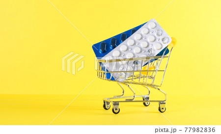 Shopping cart with pills on a yellow background, closeup. Medicine concept, online shopping Shopping cart with pills on a yellow background, closeup. Medicine concept, online shopping 77982836