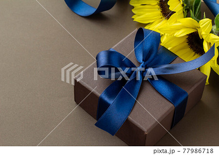 濃い青のリボンとひまわりの花とこげ茶色の無地の背景のプレゼントのイメージの写真素材