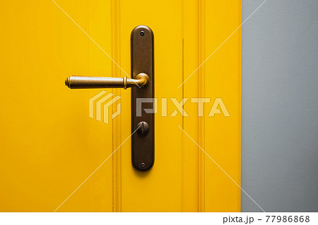 Yellow door with a bronze door handle close-up. Yellow door with a bronze door handle close-up. 77986868