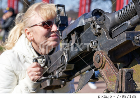 blonde woman in dark glasses shoots an anti-aircraft machine gun aiming upwards 77987138