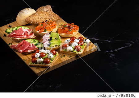 An assortment of sandwiches with fish, cheese, meat and vegetables lay on the board and a bun An assortment of sandwiches with fish, cheese, meat and vegetables lay on the board and a bun 77988186