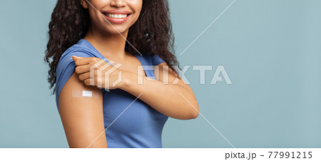 Successful covid-19 vaccination. Happy unrecognizable black woman showing arm with plaster, blue background, free space 77991215