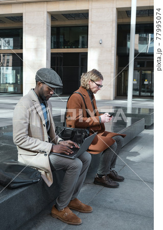 Young people using gadgets outdoors Young people using gadgets outdoors 77995074