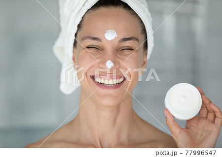 Overjoyed happy girl advertising facial skin moisturizer, showing circular jar Overjoyed happy girl advertising facial skin moisturizer, showing circular jar 77996547