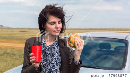 A smiling woman against a blue sky is about to eat a hamburger A smiling woman against a blue sky is about to eat a hamburger 77998877