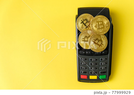 Bitcoin coins on the payment terminal on the yellow background. Bitcoin coins on the payment terminal on the yellow background. 77999929