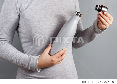 Woman in grey tee opening grey insulated bottle on yellow background 78002510