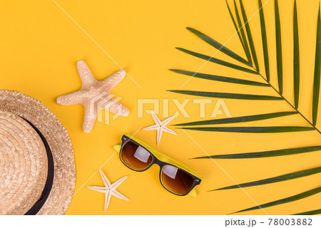 Beach accessories: glasses and hat with shells and sea stars on a colored background 78003882