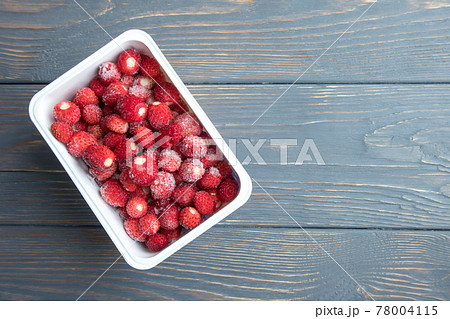 Frozen strawberries in a container on a wooden background with space for text. The concept of preparing products for future use. Frozen strawberries in a container on a wooden background with space for text. The concept of preparing products for future use. 78004115