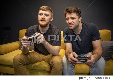 male homosexual couple passionately playing video game holding console joysticks 78004403