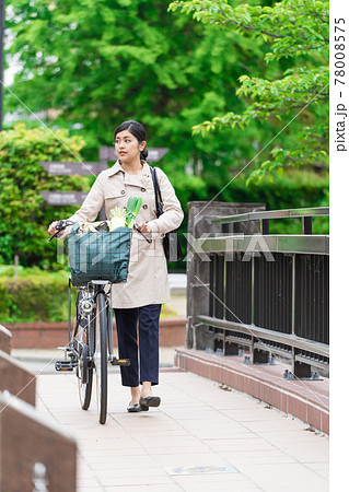 買い物袋を自転車のカゴ 籠 に入れて引いて歩く若い女性 の写真素材