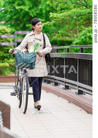 買い物袋を自転車のカゴ 籠 に入れて引いて歩く若い女性 の写真素材