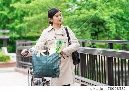 買い物袋を自転車のカゴ（籠）に入れて引いて歩く若い女性  78008582