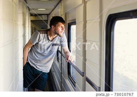 Handsome young caucasian man with a beard, looks outside of the train's window Handsome young caucasian man with a beard, looks outside of the train's window 78010767