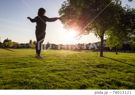Adventurous White Caucasian Adult Woman walking on a Slackline Adventurous White Caucasian Adult Woman walking on a Slackline 78013121