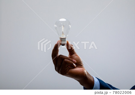 Close up of african american businessman holding light bulb against grey background 78022006