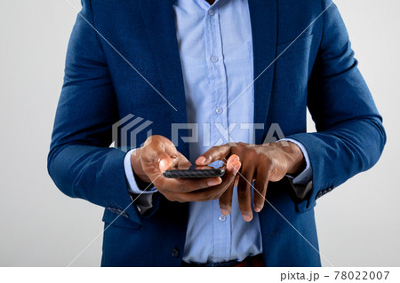 Mid section of businessman using fingerprint scanner on smartphone against grey background 78022007