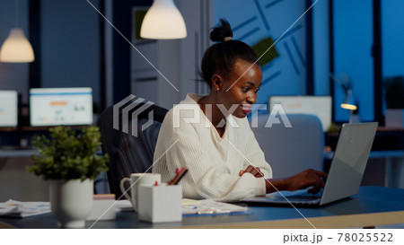 Happy african freelancer reading tasks on laptop working overtime 78025522