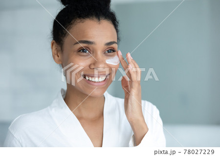 Smiling Afro American woman in bathrobe spreading moisturizing collagen cream 78027229