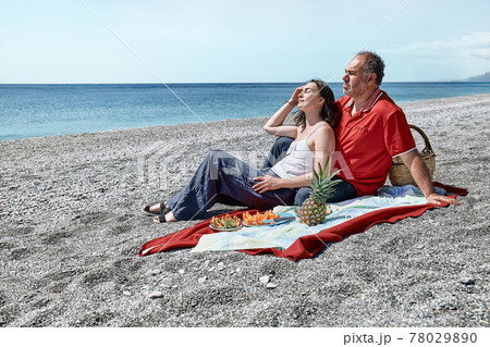 Middle aged couple having a picnic at the seaside with fresh exotic fruit. Spring, summer time lifestyle, love dating concept. 78029890