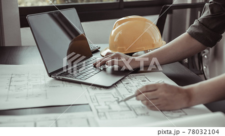 Young man with a laptop plotting a system of building structures in blueprints, Architects or engineers are designing buildings using computers to calculate the physical structure to be correct. Young man with a laptop plotting a system of building structures in blueprints, Architects or engineers are designing buildings using computers to calculate the physical structure to be correct. 78032104