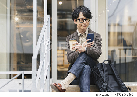 テイクアウトカップとスマホを持ったメガネをかけた30代前半の男性 テイクアウトカップとスマホを持ったメガネをかけた30代前半の男性 78035260
