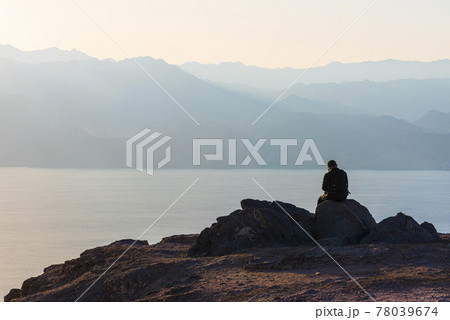 A man sits on a high mountain cliff and overlooks the horizon. A concept for hope, peace, power, soul searching 78039674
