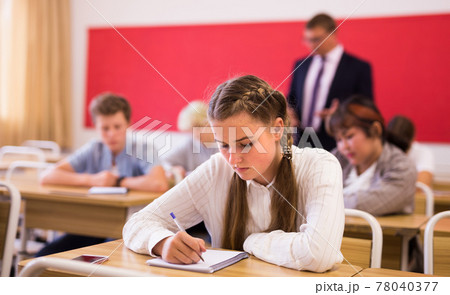 Focused teenage schoolgirl writing lectures in classroom Focused teenage schoolgirl writing lectures in classroom 78040377