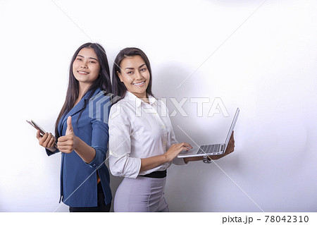 Two beautiful Asian business women standing in a modern collaborative office, smiling, looking at the screen of a tablet device, preparing a presentation about electronic devices. Cutting edge 78042310