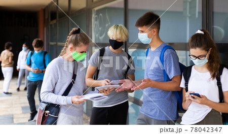 Group of students in protective masks discuss past lessons at a college on street 78042347
