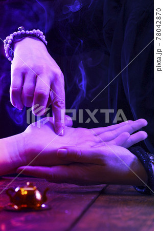 Witch is a fortune teller reading good luck close-up. Fortune teller guides the lines on the client's hand in neon light 78042870