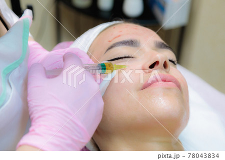 The doctor gives injections of blood plasma into the face of a young girl. 78043834