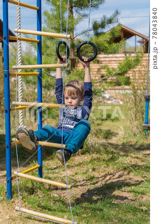 A blonde-haired child is playing on the playground, hanging on rings A blonde-haired child is playing on the playground, hanging on rings 78043840