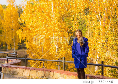 A young girl walks in the autumn park, stands behind a tree. 78044461