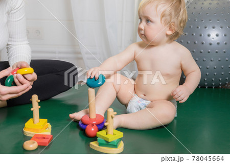 The kid sits on the rug, plays with his mother, collects a pyramid. The kid sits on the rug, plays with his mother, collects a pyramid. 78045664
