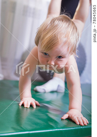 Mom holds the baby by the legs, the baby walks on the rug in her arms. Mom holds the baby by the legs, the baby walks on the rug in her arms. 78045665