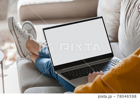 Young woman using laptop screen blank, mock up lying on sofa at home 78046598