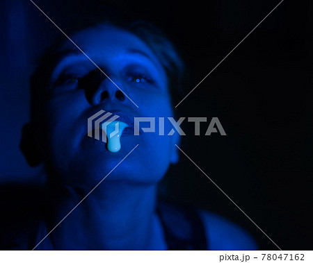A thick white liquid flows down the lips of a young European girl. Dripping down. Ultraviolet, blue light. Close-up portrait. Spit out. A thick white liquid flows down the lips of a young European girl. Dripping down. Ultraviolet, blue light. Close-up portrait. Spit out. 78047162