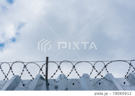 High metal corrugated wall with barbed wire and gray sky High metal corrugated wall with barbed wire and gray sky 78060912