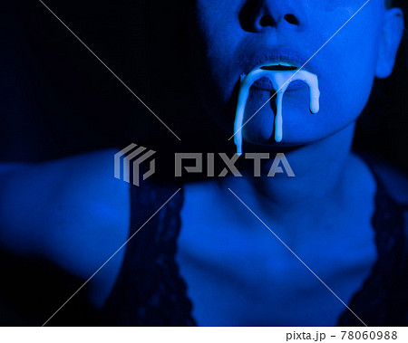 A thick white liquid flows down the lips of a young European girl. Dripping down. Ultraviolet, blue light. Close-up portrait. Spit out. A thick white liquid flows down the lips of a young European girl. Dripping down. Ultraviolet, blue light. Close-up portrait. Spit out. 78060988