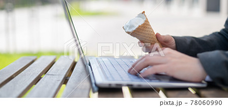 Close-up of the hands of a business woman on a laptop keyboard on a summer terrace. Office clerk eating an ice cream cone outdoors. Cropped photo. Vanilla frozen yogurt in a waffle cup. Close-up of the hands of a business woman on a laptop keyboard on a summer terrace. Office clerk eating an ice cream cone outdoors. Cropped photo. Vanilla frozen yogurt in a waffle cup. 78060990