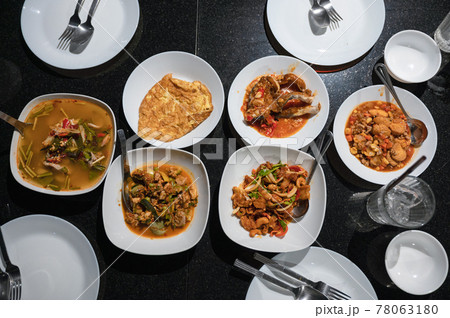 Variety of Thai food with spicy soup, fried fish, tofu, chicken curry, salad and silverware on dining table at dinner 78063180